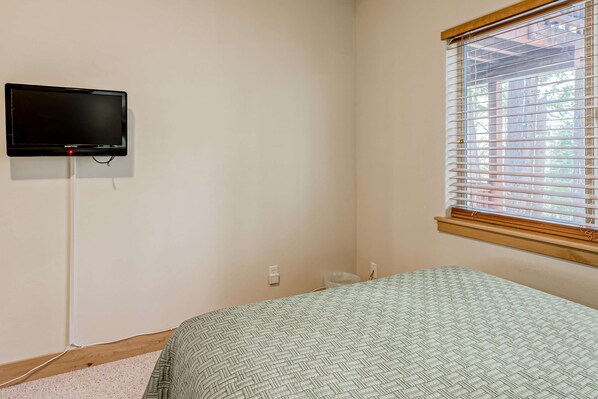 A bedroom with a bed, a wall-mounted TV, a window with blinds, and a power outlet. - Inviting spacious home with fireplace, deck, hot tub, full kitchen, & W&D (South Lake Tahoe)