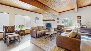 Un salon spacieux doté d’une cheminée, de poutres apparentes en bois et de grandes fenêtres.
