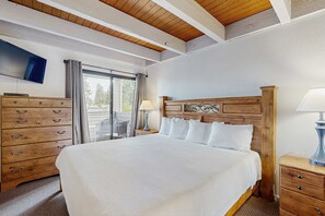 A hotel room with a large bed, wooden headboard, a TV mounted on the wall, a dresser, and a window with curtains. - Lakeland Village is the ultimate jumping off point for mountain adventure (South Lake Tahoe)