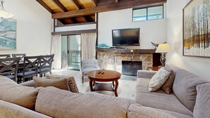 Una sala de estar con chimenea de piedra, televisor, sofá y comedor con sillas.