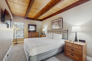 Ein Schlafzimmer mit einem großen Bett, hölzernen Nachttischen, einem Spiegel und einem Fenster mit Jalousien.