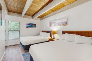 Ein Hotelzimmer mit zwei Betten, Holzbalkendecke, einem Fenster mit Jalousien und zwei an der Wand hängenden Bildern.