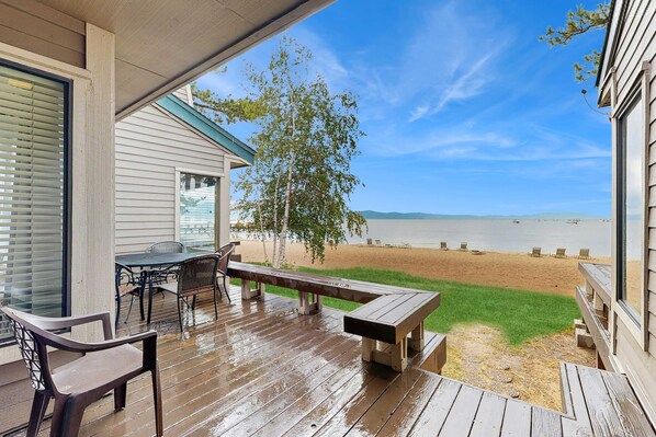 Eine Holzterrasse mit Tisch, Stühlen und einer Bank, mit Blick auf Strand und Meer.