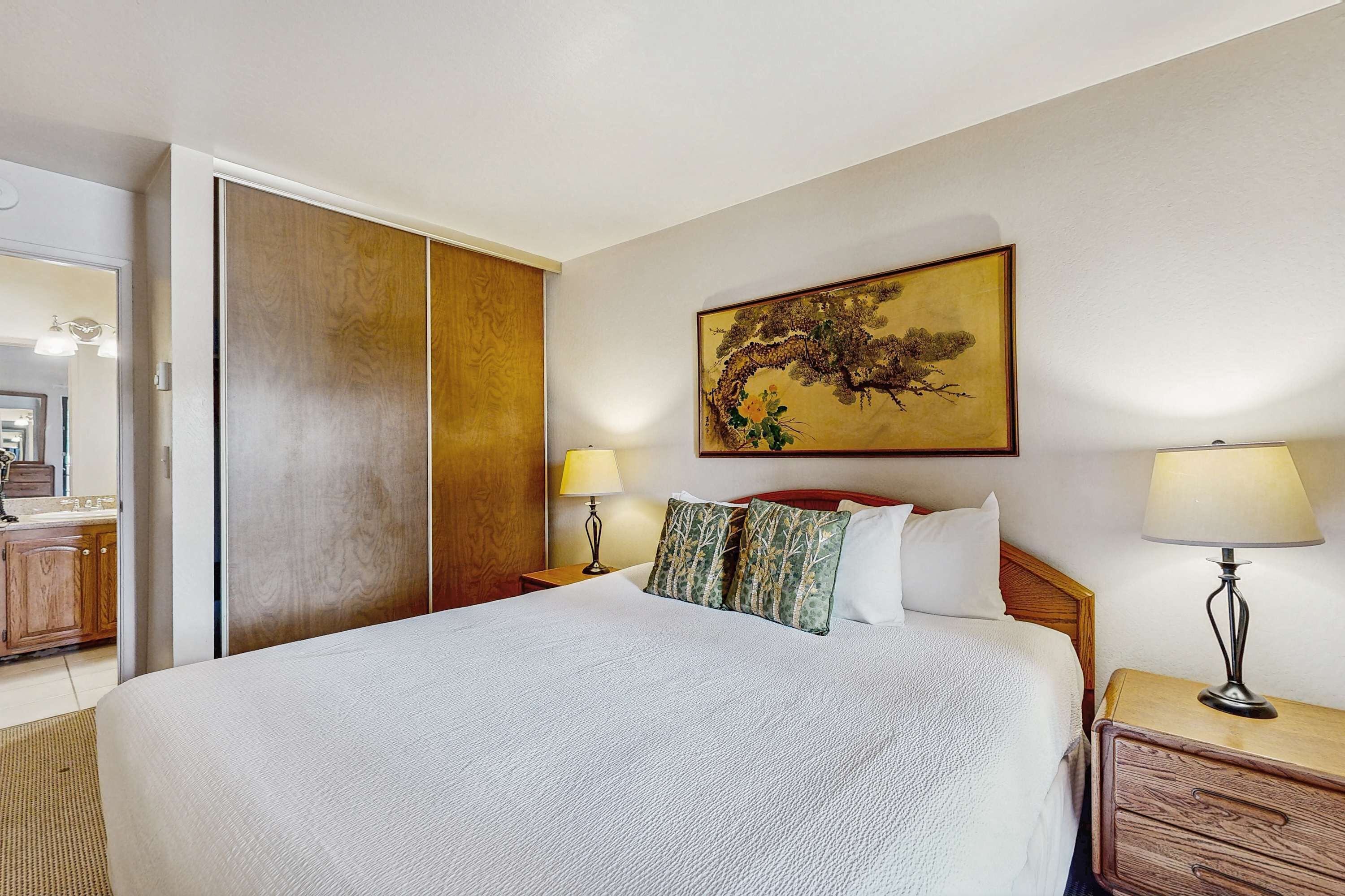 Camera d'albergo con un letto grande, un armadio in legno, un quadro appeso al muro, due lampade da comodino e un comodino in legno.