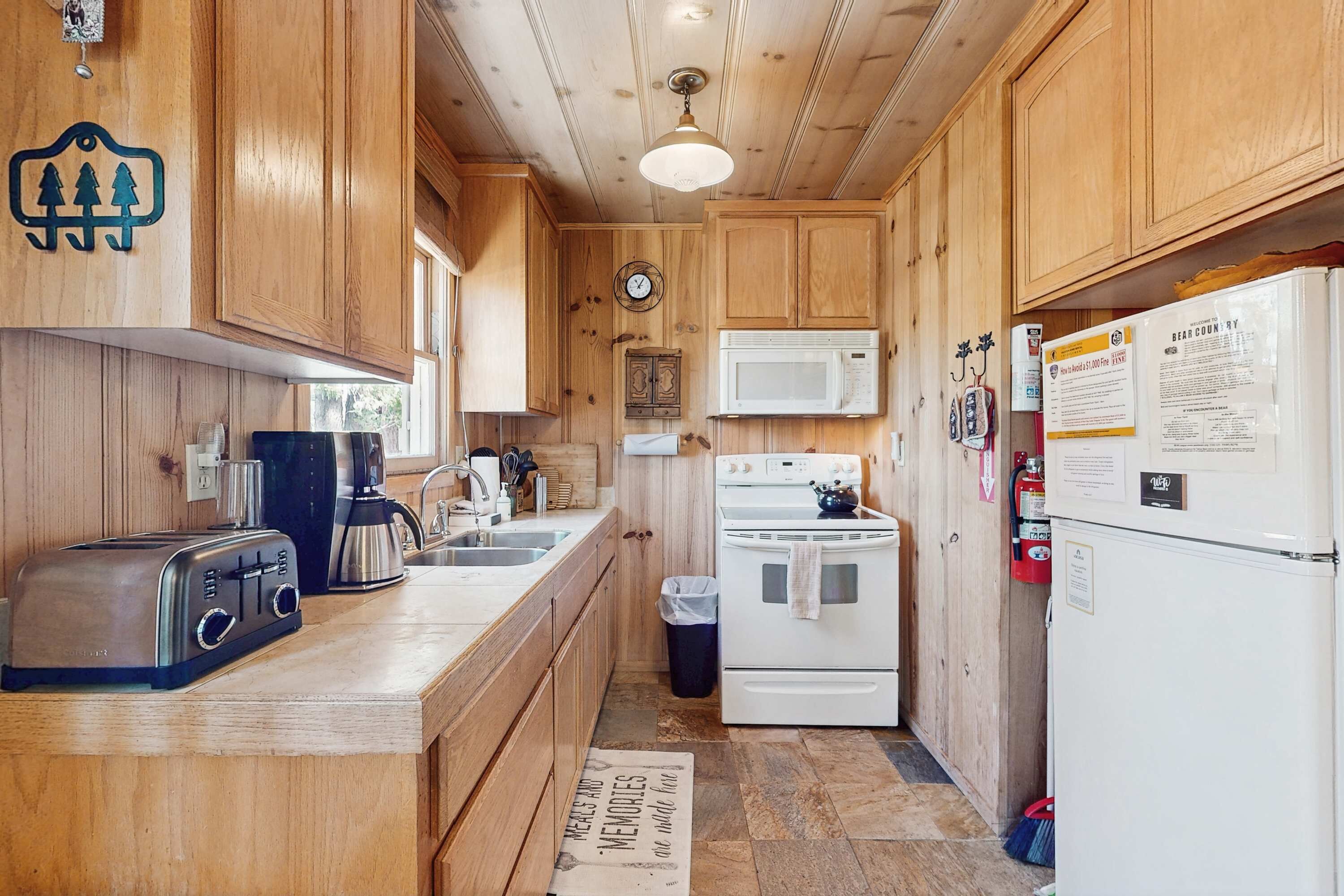 Une cuisine compacte avec des meubles en bois, un four à micro-ondes, une cuisinière, un grille-pain et une horloge murale.