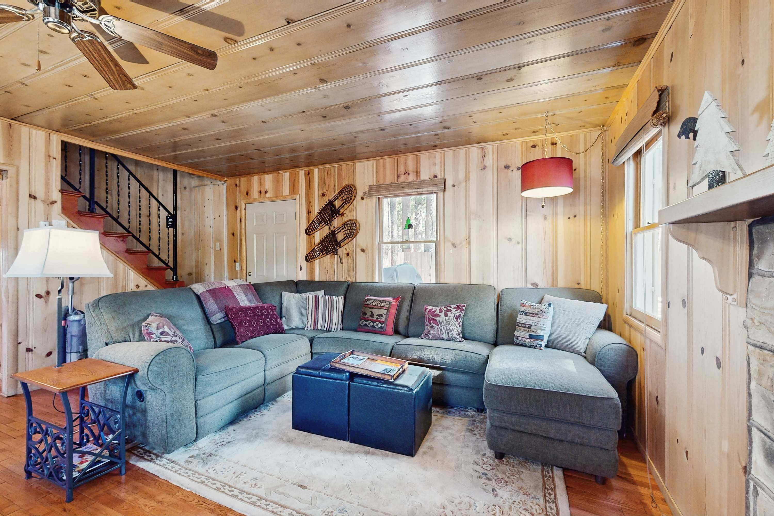 A cozy living room with a sectional sofa, a coffee table, a wooden staircase, and a fireplace.