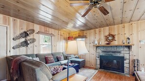 Interior acogedor de una cabaña con chimenea, paredes de madera, ventilador de techo y un sofá.