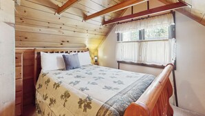 Un dormitorio con techo de madera, una cama con colcha estampada, una mesita de noche, una ventana con cortinas y un cabecero de madera.