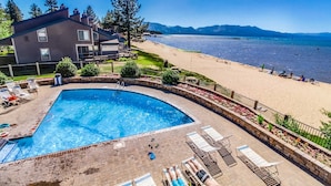 A pool area with lounge chairs, a swimming pool, and a view of the beach and mountains. - Lakeside living with wonderful amenities & activities (South Lake Tahoe)