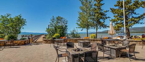 An outdoor patio with tables and chairs, overlooking a body of water and mountains.