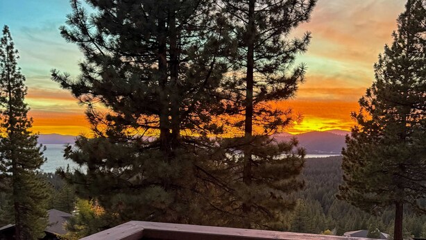 A scenic view of a forested area with a sunset over a body of water, likely from a high vantage point. - Spacious home with incredible views, full kitchen, shared  pool & tennis courts (Incline Village)