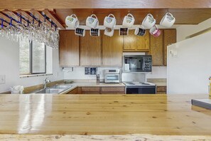 Eine Küche mit Holzausstattung, einer Arbeitsplatte, einem Spülbecken, einer Mikrowelle, einem Toaster und aufgehängten Tassen.