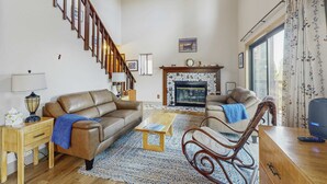 A living room with a staircase, leather sofas, a fireplace, and a large window with curtains. - Spacious home with incredible views, full kitchen, shared  pool & tennis courts (Incline Village)