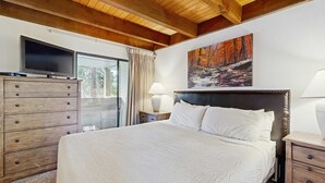 Een slaapkamer met een bed, een houten dressoir, een televisie en een schilderij van een bos.