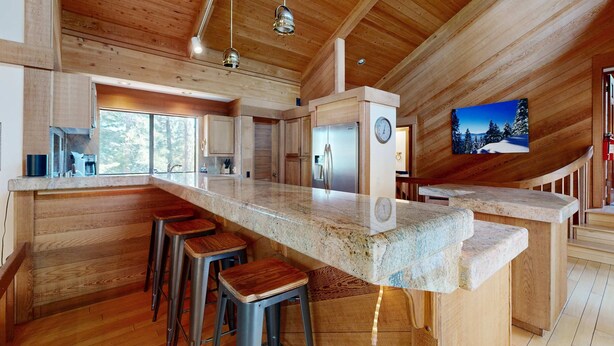 Una cucina con mobili in legno, una grande isola con sgabelli, un frigorifero e un quadro raffigurante un paesaggio innevato.