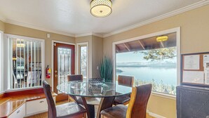 A dining area with a glass table, wooden chairs, a view of a lake, and a bulletin board on the wall. - Luxury home with game room, sauna, and stunning lake views (Zephyr Cove)