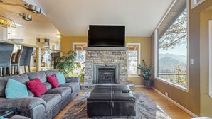 A modern living room with a stone fireplace, a large flat-screen TV, and a sofa with colorful cushions. - Luxury home with game room, sauna, and stunning lake views (Zephyr Cove)