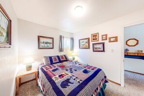 A bedroom with a bed, a nightstand with a lamp, a dresser, and framed pictures on the wall.