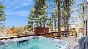 Een hottub op een houten terras met uitzicht op een chalet en bomen.