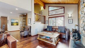 Een ruime woonkamer met een houten plafond, een open haard, een stenen muur en een beerbeeld.