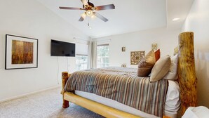 Une chambre à coucher avec un lit, un ventilateur de plafond, une télévision et une fenêtre.