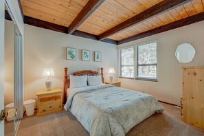 A bedroom with a wooden ceiling, a bed with a patterned bedspread, two bedside lamps, a wooden nightstand, a wooden wardrobe, and a window with blinds. - Rustic Kingswood Village getaway with shared pool, patio, & wood-burning fireplace (Kings Beach)
