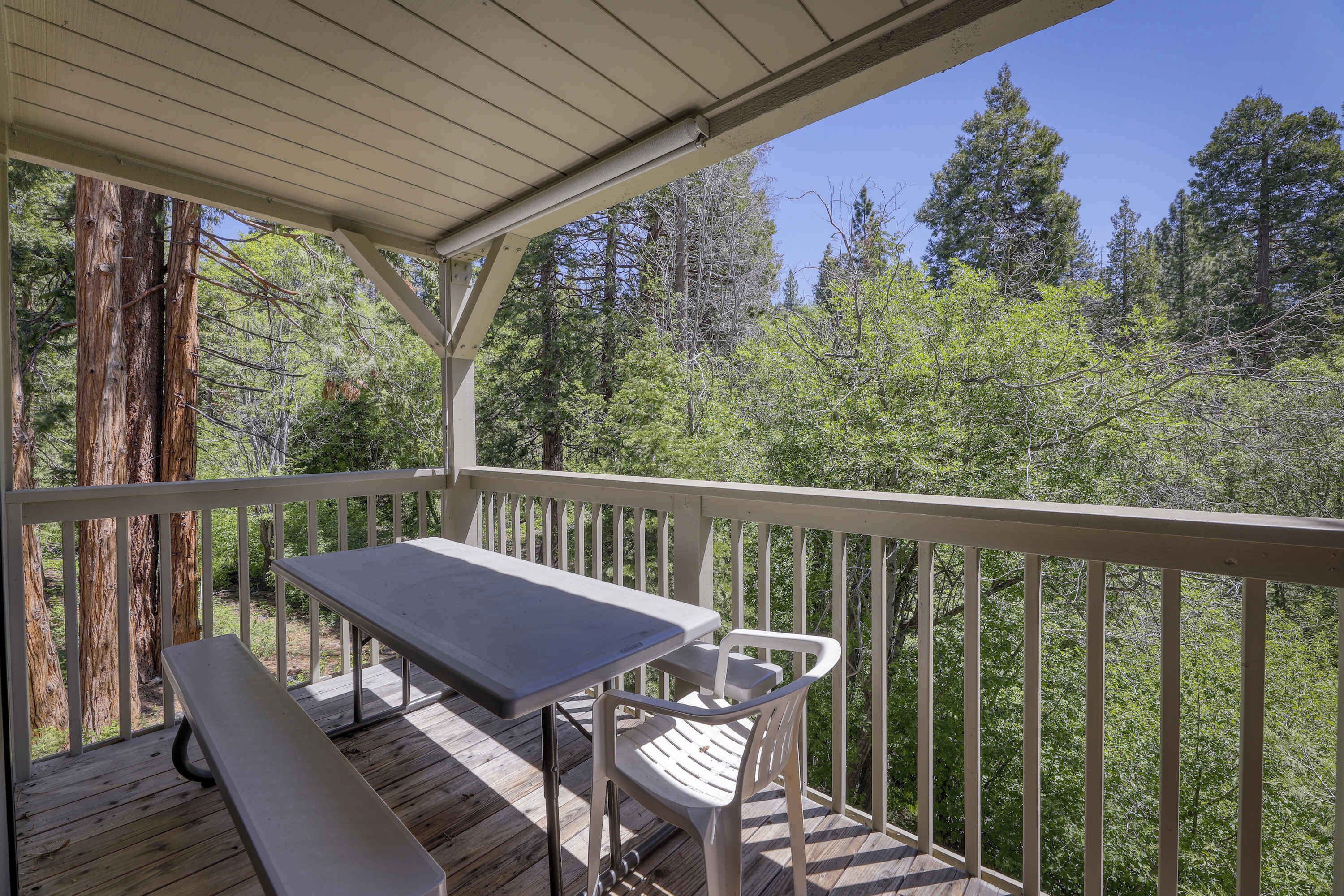 A wooden deck with a table and chairs, surrounded by a railing, overlooking a forested area.