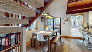Un interior moderno con una escalera de madera, una zona de comedor con un banco y una estantería.