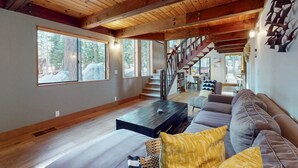 Amplia sala de estar con techo de madera, ventanas grandes, una escalera y un sofá moderno.