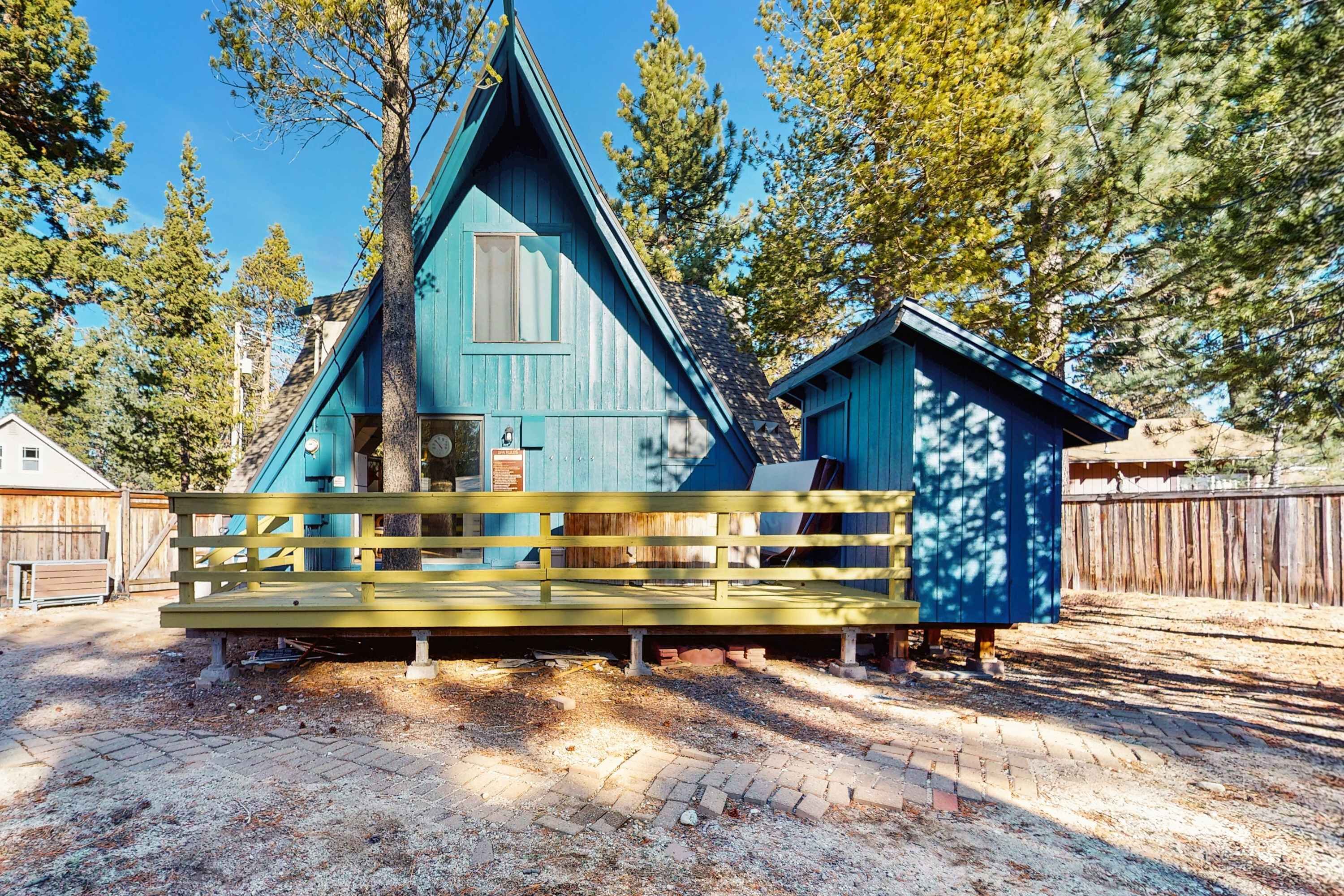 Une cabane bleue avec un banc en bois devant, entourée d’arbres.