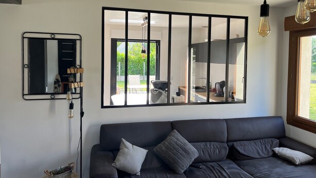 A modern living room with a dark sofa, a large mirror, and a view of the outdoor patio. - Villa "Quiet House near Dinan" with Private Terrace, Garden, and Wi-Fi (Aucaleuc)