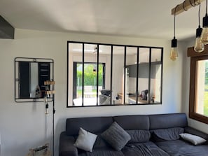 Un salon moderne avec un canapé foncé, un grand miroir et une vue sur la terrasse extérieure.