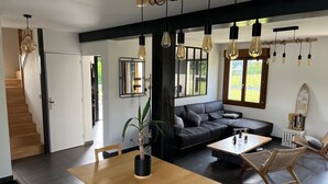 A modern living space with a staircase, a dining area, a sofa, and a large window. - Villa "Quiet House near Dinan" with Private Terrace, Garden, and Wi-Fi (Aucaleuc)