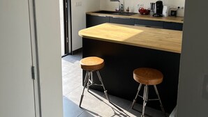 A modern kitchen with a wooden countertop, two stools, and pendant lights. - Villa "Quiet House near Dinan" with Private Terrace, Garden, and Wi-Fi (Aucaleuc)