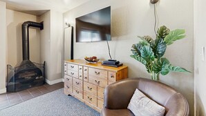 Ein Wohnzimmer mit Kamin, Fernseher, Holzschrank, braunem Ledersessel und einer großen Zimmerpflanze.