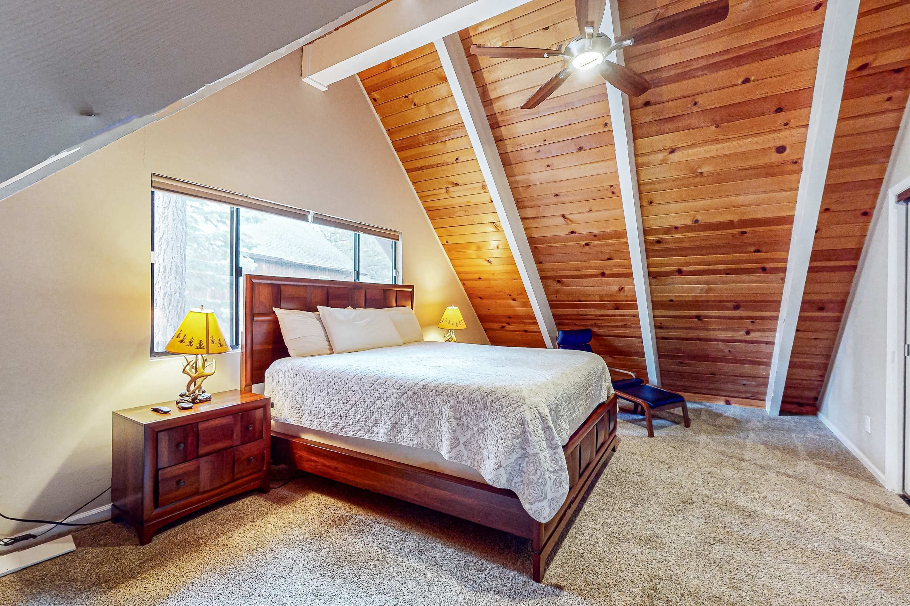 Een slaapkamer met een schuine kap, een bed, een nachtkastje, een lamp en een stoel.