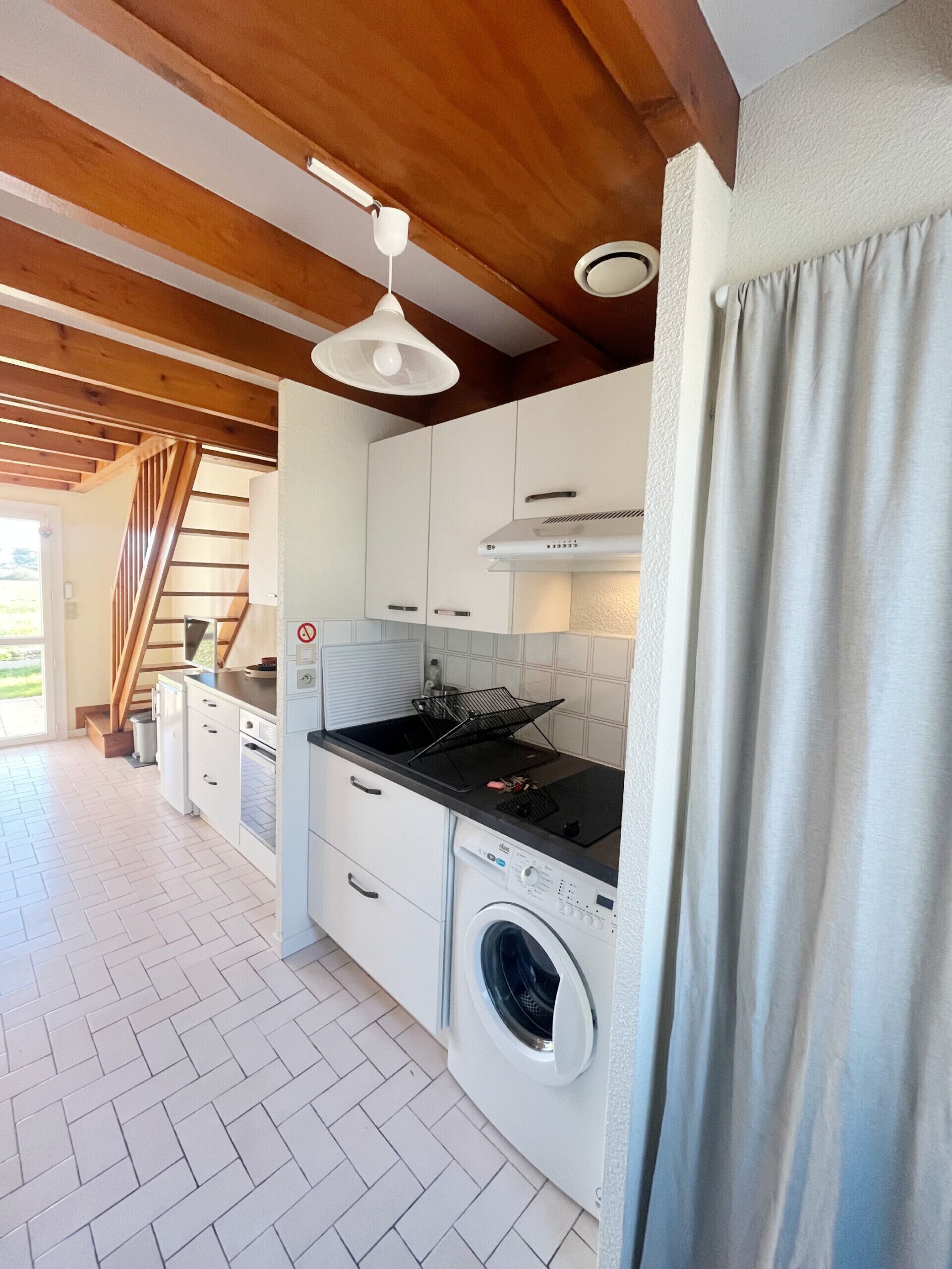 A kitchen with white cabinets, a black countertop, a built-in washing machine, and a wooden ceiling.