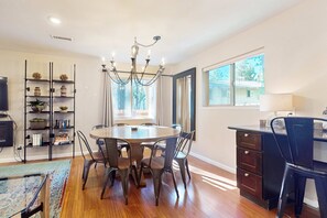 A dining area with a round table, chairs, a chandelier, a bookshelf, and a window with a view. - Charming dog-friendly home with a private hot tub & large fenced yard (South Lake Tahoe)