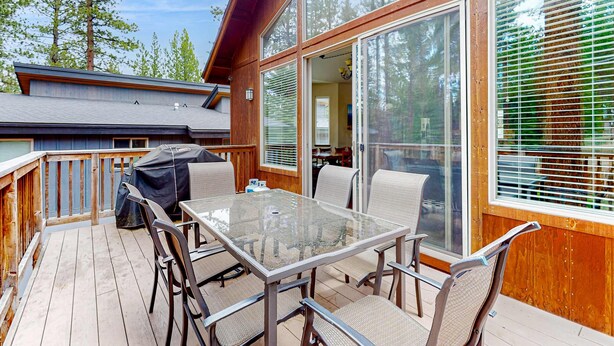 Une terrasse dotée d’une table et de chaises à plateau en verre, d’un barbecue et offrant une vue sur la forêt environnante.