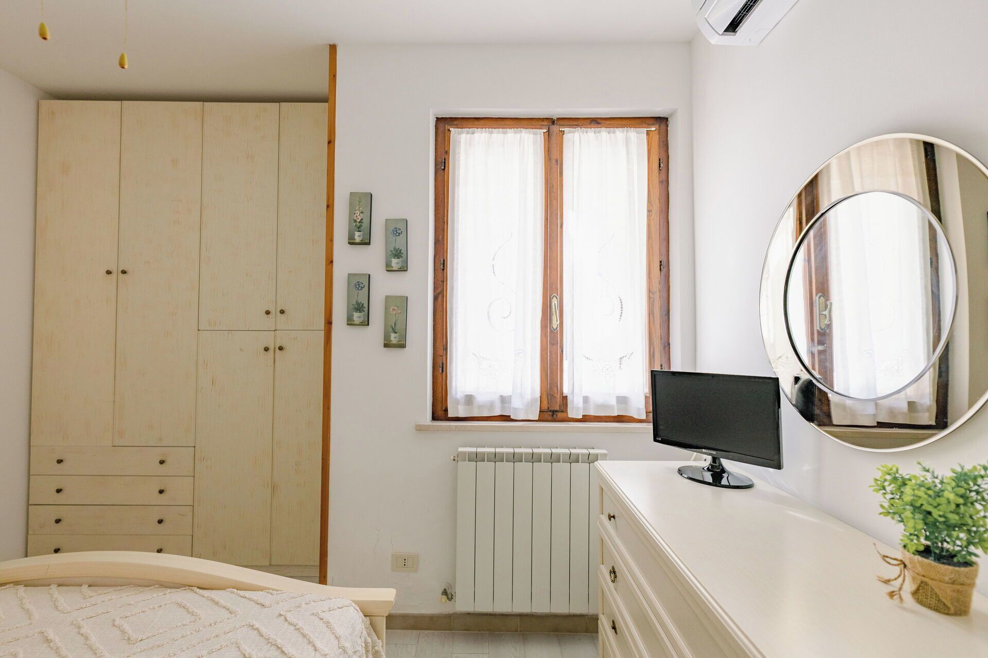 A bedroom with a bed, a dresser, a mirror, a window with curtains, and a radiator.