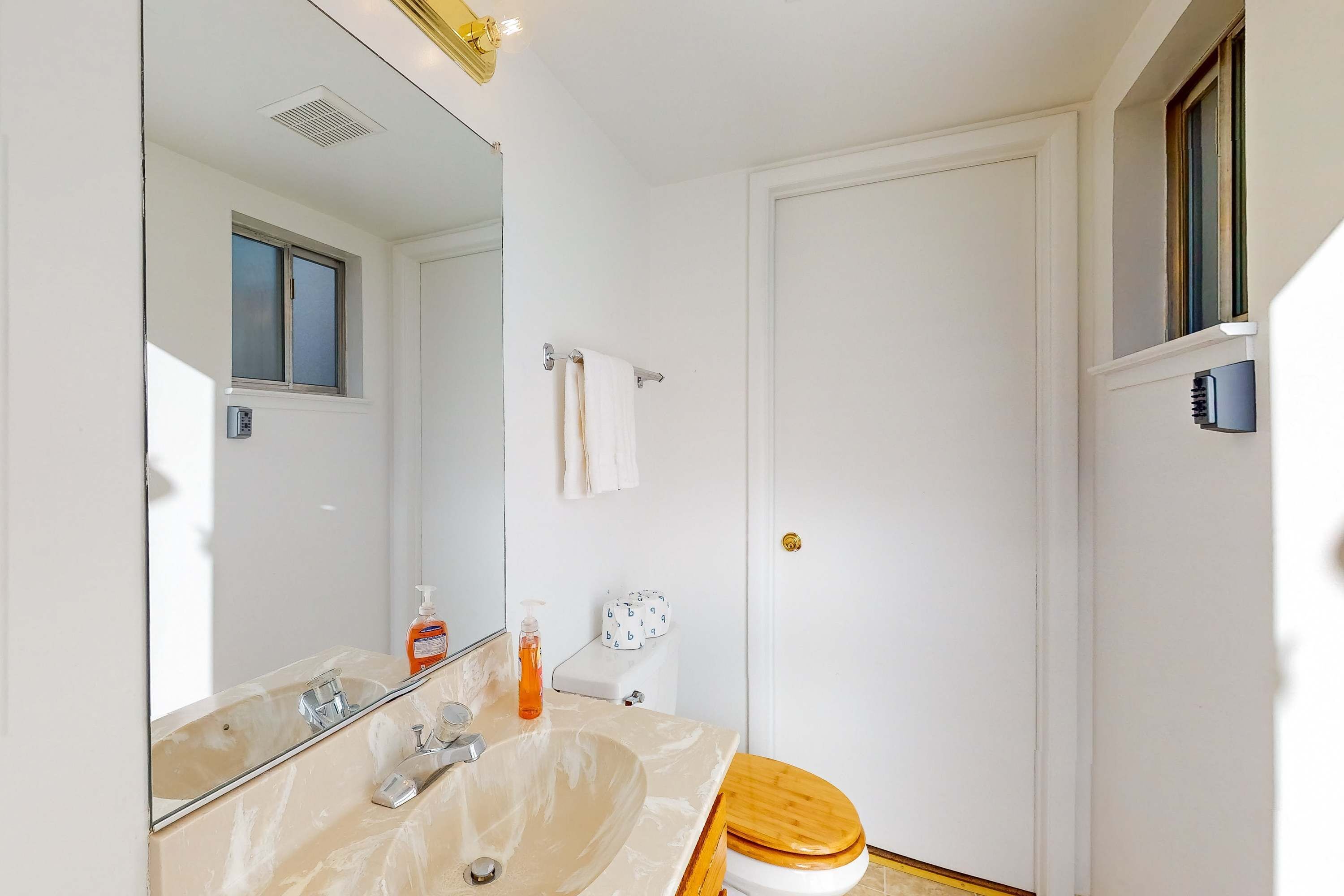 Un baño con lavamanos, espejo, inodoro y ventana.