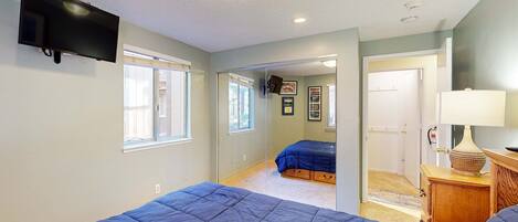 A bedroom with two beds, a TV, and a door leading to another room.