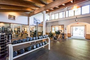Ein Fitnessstudio mit Krafttrainingsgeräten, Spiegeln und einem großen Fenster.