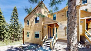 A two-story wooden cabin with a staircase leading to the entrance, surrounded by trees. - Sophisticated Gold Bend Getaway | Fireplace | Free Ski Shuttle, Pool, Hot Tub (Northstar - Truckee)