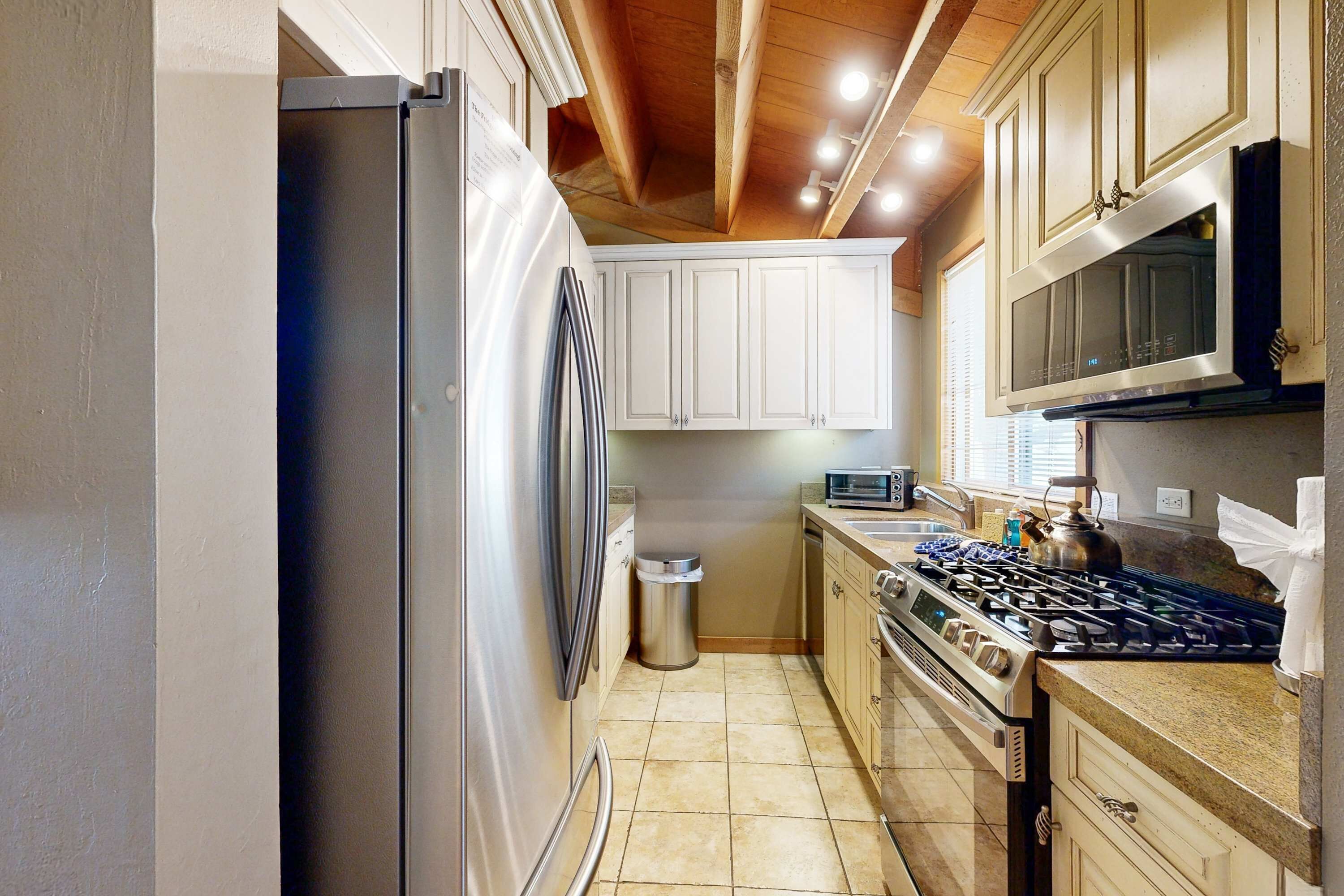A compact kitchen with a stainless steel refrigerator, a microwave, a gas stove, and white cabinets.