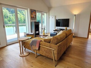 Ein Wohnzimmer mit einer Couch, einem Fernseher und Blick auf einen Balkon.