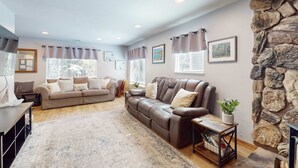 A living room with a brown leather sofa, a coffee table, a rug, and a stone wall. - Tahoe Getaway: Spacious Deck, Fireplace & Family-Friendly (South Lake Tahoe)