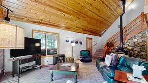 Ein Wohnzimmer mit Holzboden, einem Fernseher, einem Kamin aus Stein, einem Ledersofa und einer Treppe.