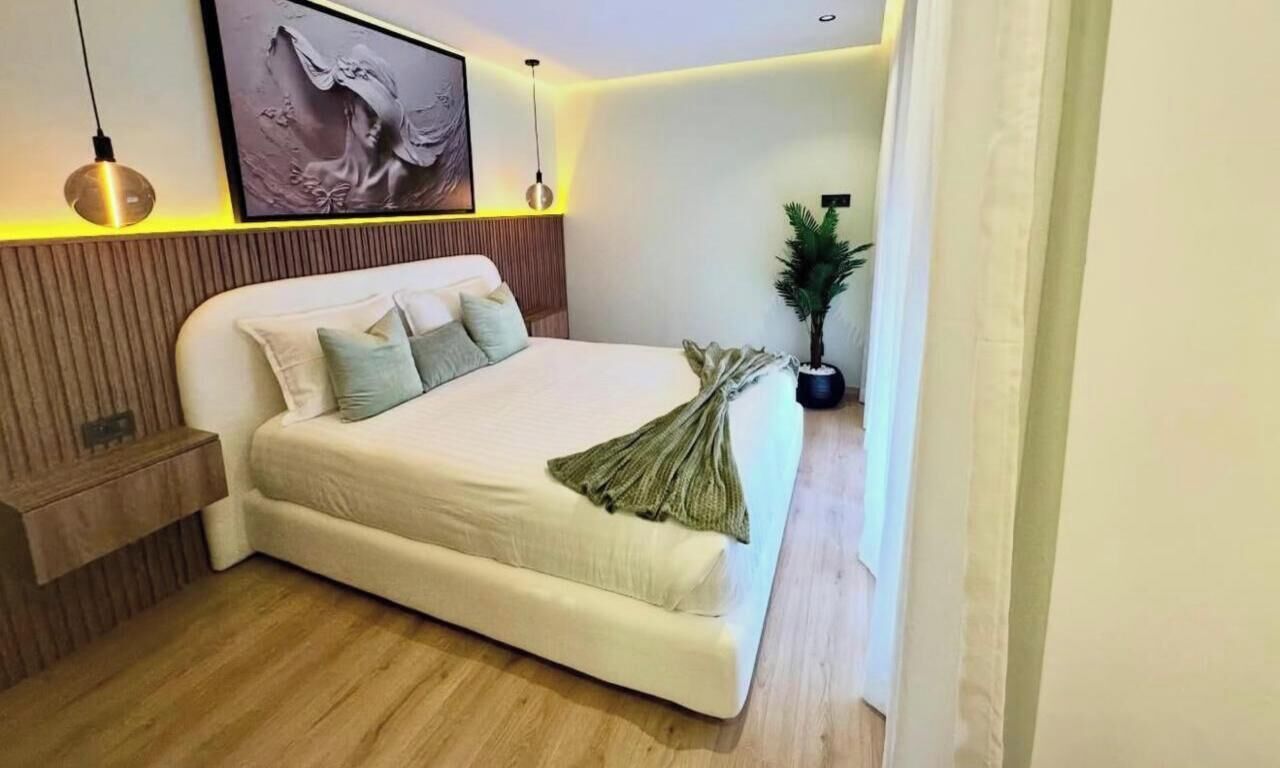 Quarto moderno com uma cama grande, painéis de madeira, uma planta em vaso e uma obra de arte emoldurada na parede.