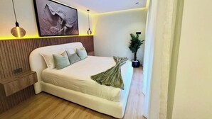 Une chambre à coucher moderne avec un grand lit, un lambris en bois, une plante en pot et une œuvre d’art encadrée accrochée au mur.